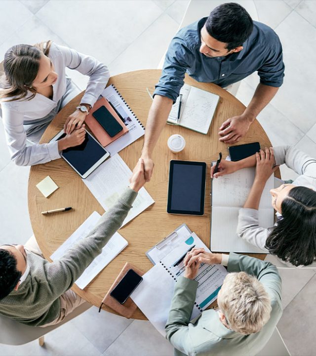 meeting-handshake-overhead-with-business-team-sitting-around-table-office-work-partnership-thank-you-welcome-with-male-colleagues-shaking-hands-agreement-b2b-deal